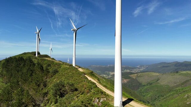 Dynamic drone pass beside a wind turbine, revealing a row of renewable energy towers across an Asturian coastal ridge.
