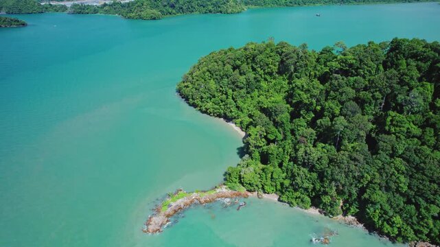 Scenic aerial orbit revealing an unspoiled tropical island with lush rainforest, rocky coastline, tranquil lagoon waters, and a hidden white sand beach perfect for travel and nature productions.