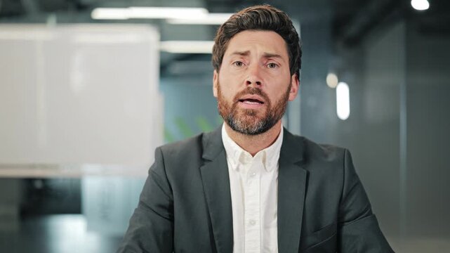 Confident business professional communicates ideas. Explains concepts using verbal delivery and expressive hand gestures online call. Modern office setting provides contemporary backdrop.