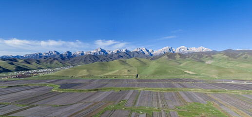 Naklejka premium Maya Snow Mountain Rising Above Grasslands and Farmland, Gansu, China.