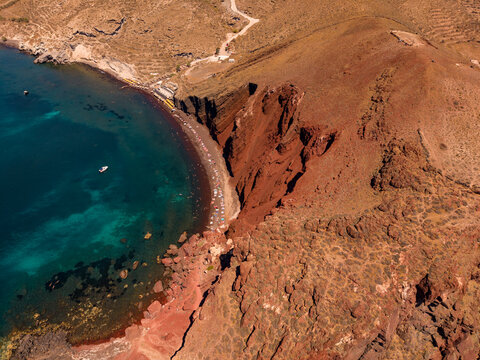 Aerial drone view of tourists sunbathing on Red Beach below red volcanic rock cliffs in Santorini Greece