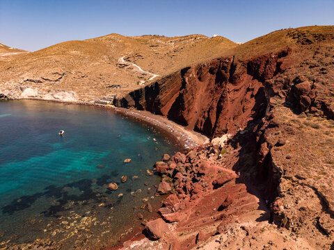 Aerial drone shot of Red Beach cove with turquoise water and steep red volcanic cliffs in Santorini Greece