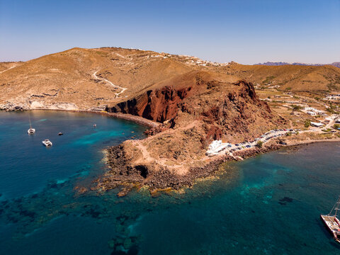 Wide aerial drone shot of Red Beach bay with yachts and red volcanic headland in Santorini Greece