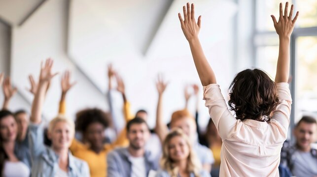 Participants in a modern workshop raising hands, engaging with a female presenter, showing active learning and participation