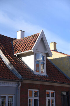 A red brick house with red roof tiles and a white roof dormer with open window. Taken in Odense, Denmark. 