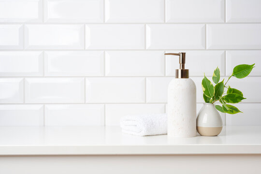 Soap dispenser and folded fresh towel on table in bathroom with copy space over white ceramic tile background
