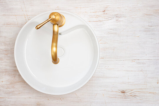 Top view of empty white ceramic sink with golden color vintage faucet on bleached wood background