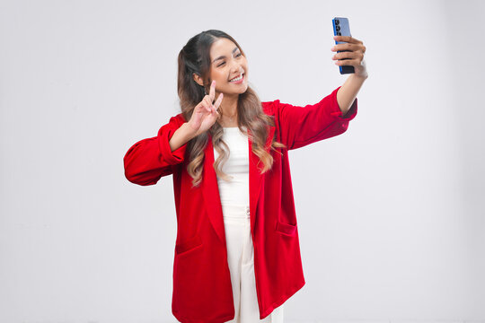 Excited Asian woman in red jacket holding a smartphone and doing video call or selfie pose.