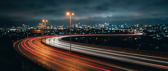 Long exposure night photography of car light trails on winding highway with city skyline © StoryPixelStudio