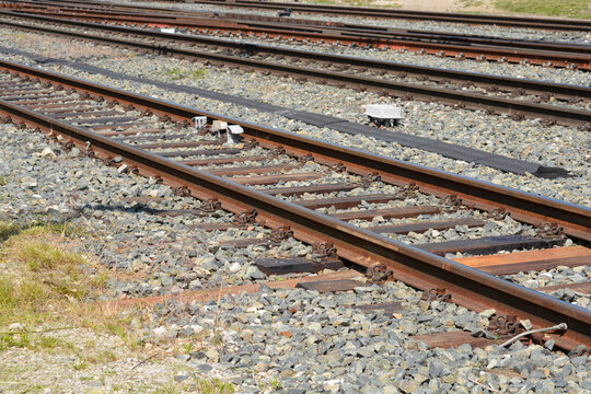 A high angle view of multiple empty parallel rusty railway tracks with wooden sleepers on gray gravel ballast on a sunny day.