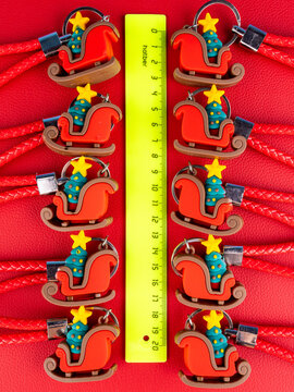 A set of 10 identical sleigh keychains, each featuring a small Christmas tree. Close-up view shows glossy red and green details, bright reflections, and a festive sparkle on a red background.