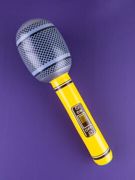 Close-up of a fun  yellow inflatable microphone toy for entertainment on a purple background.