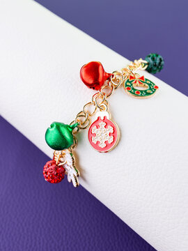 Close-up of a metallic Christmas bracelet with pendants shaped like a snowflake, holiday wreath, bells, and other festive charms.