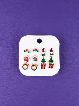 Close-up of a set of Christmas earrings featuring gnome, gift box, house, and other festive designs  on purple background