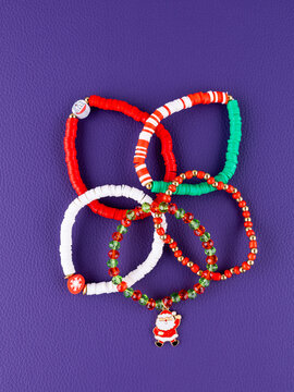Close-up of a set of red and green Christmas bracelets with pendants featuring Santa Claus,  and a Christmas tree