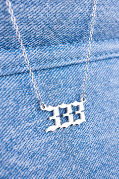 Close-up of a silver  pendant with the number 333 on a chain, set against a blue background.