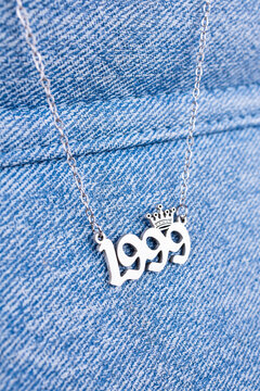 Close-up of a silver pendant with the year 1999 and a cute crown on a chain, set against a blue  background.