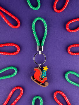 Close-up of a Christmas sleigh with a decorated tree keychain on a vibrant purple background. Festive holiday accessory 