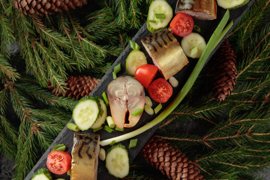 Smoked mackerel with fresh cucumbers, tomatoes and green onions on a black plate.
