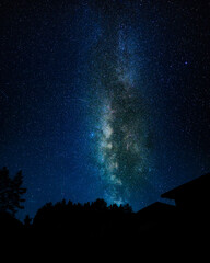 Bright Milky Way core above forest and cabin silhouettes on a starry night © Earthly Shots