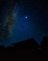 Starry summer night sky with the faint Milky Way over a rural rooftop silhouette © Earthly Shots