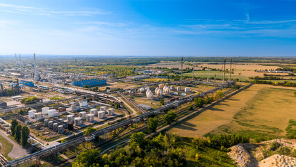 Plakat High aerial view of large oil refinery complex adjacent to countryside.. Extensive industrial plant with spherical tanks, pipe racks, green trees, dry yellow fields, clear sky.