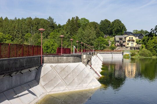 Modern concrete dam wall with red street lamps standing along calm waters at Lake B&uuml;tgenbach in Belgium
