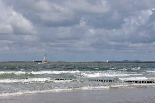 Scenic seascape view of choppy waves crashing on Cadzand beach (The Netherlands) with sailboats navigating the horizon