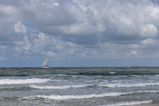Lonely sailboat navigating through choppy ocean waters under dramatic cloudy skies off the coast of Cadzand - The Netherlands