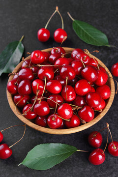 Fresh ripe sweet cherries in rustic wooden bowl on black stone textured background with copy space for text. Juicy organic summer fruit, red berries, healthy seasonal food, farm harvest