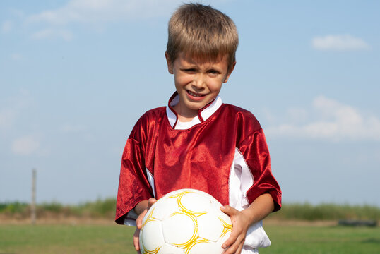 Young Boy in Red Soccer Jersey Holding a Football Outdoors