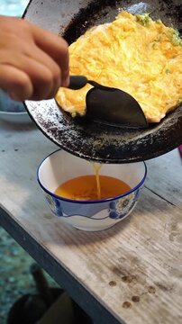 Cooking Thai traditional omelet with edible flowers (Khai Jiew Dok Khajon). Whisking eggs with fresh cowslip creeper flowers (telosma cordata), pouring into hot oil in a wok, flipping until golden flu