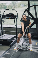 Fototapeta premium Asia man performing battle rope exercise or exercise with sled pull in gym