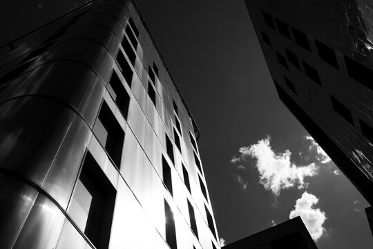 From below, an upward view follows a curved skyscraper facade in monochrome, where vertical windows climb toward a single cloud, sharpening contrast against the open sky