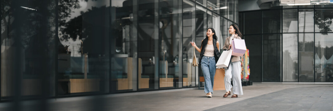 Two Asian women walking outside shopping mall with paper bags for Black Friday sale deals
