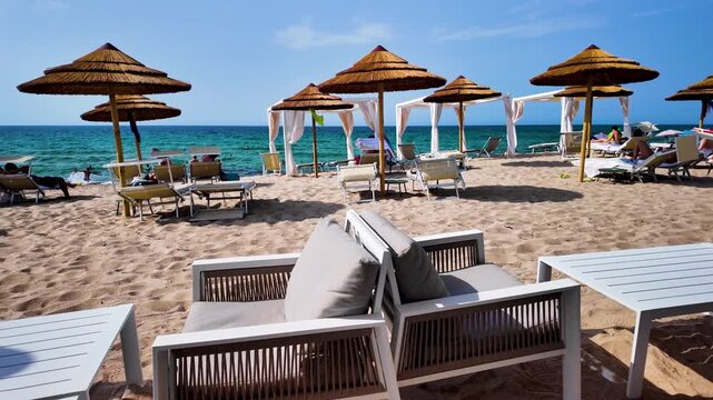 Panoramic view of the beach with umbrellas and wooden armchairs overlooking the turquoise Mediterranean Sea in sunny Italy