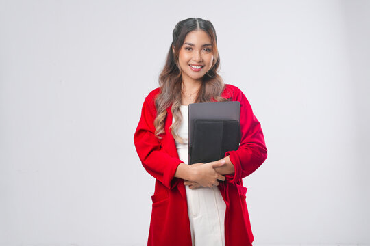 Confident Asian young woman in red jacket holding a document book and laptop while smiling.