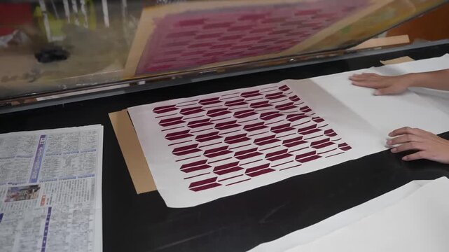 Squeegee pulls crimson ink across the mesh then the frame lifts to reveal a crisp printed motif on the sheet beneath