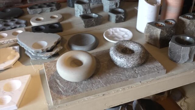 Finished granite tableware including sake cups, plates and ring shaped dishes displayed along a wooden workshop bench