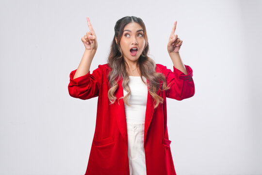 Surprised young Asian woman in a red jacket pointing to the copy space above her.