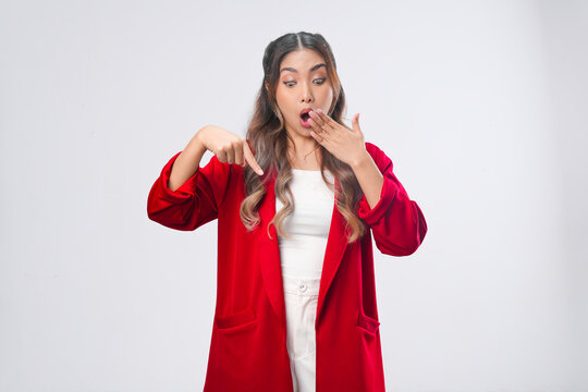 Shocked young Asian woman in a red jacket is pointing to the copy space below.