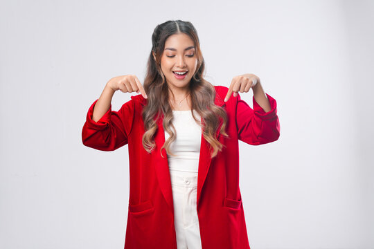 Smiling young Asian woman in a red jacket pointing to the copy space below.