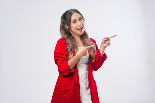 Joyful young Asian woman in a red jacket pointing to the copy space beside her.