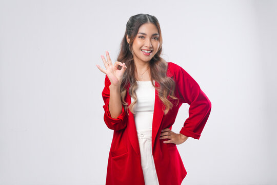 Attractive young Asian woman in a red jacket is giving okay good hand gesture.