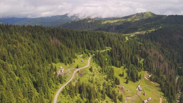 Wide aerial view of a serpentine mountain road, wooden cabins, and dense pine forest in Kotlovi, near Montenegro Kosovo border.