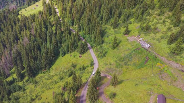Aerial view of a white camper van driving along a serpentine mountain road past rural cabins in Kotlovi, near Montenegro Kosovo border.