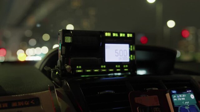 Illuminated taxi meter reading 500 yen on a dashboard with night city lights in Japan
