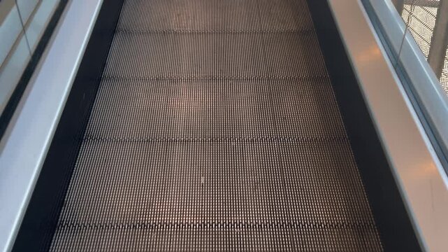 Abstract architectural view looking upward along an empty escalator with parallel handrails and textured metal steps. Modern transportation, geometry and urban interior concept. 4K.