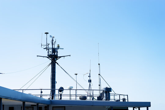 A ship mast with multiple antennas and rigging rises above the deck, set against a clear blue sky that conveys calm, openness and nautical industry details for maritime and technology themes.
