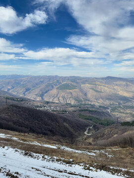 Mountain landscape with winding road and snow patches under bright blue sky.